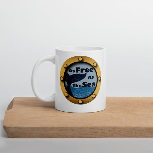 White mug with a whale and sea graphic and 'Free as the Sea' text on a wooden surface.