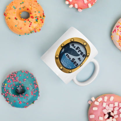 White mug with a whale and sea graphic and 'Free as the Sea' text surrounded by colorful donuts on a light blue background