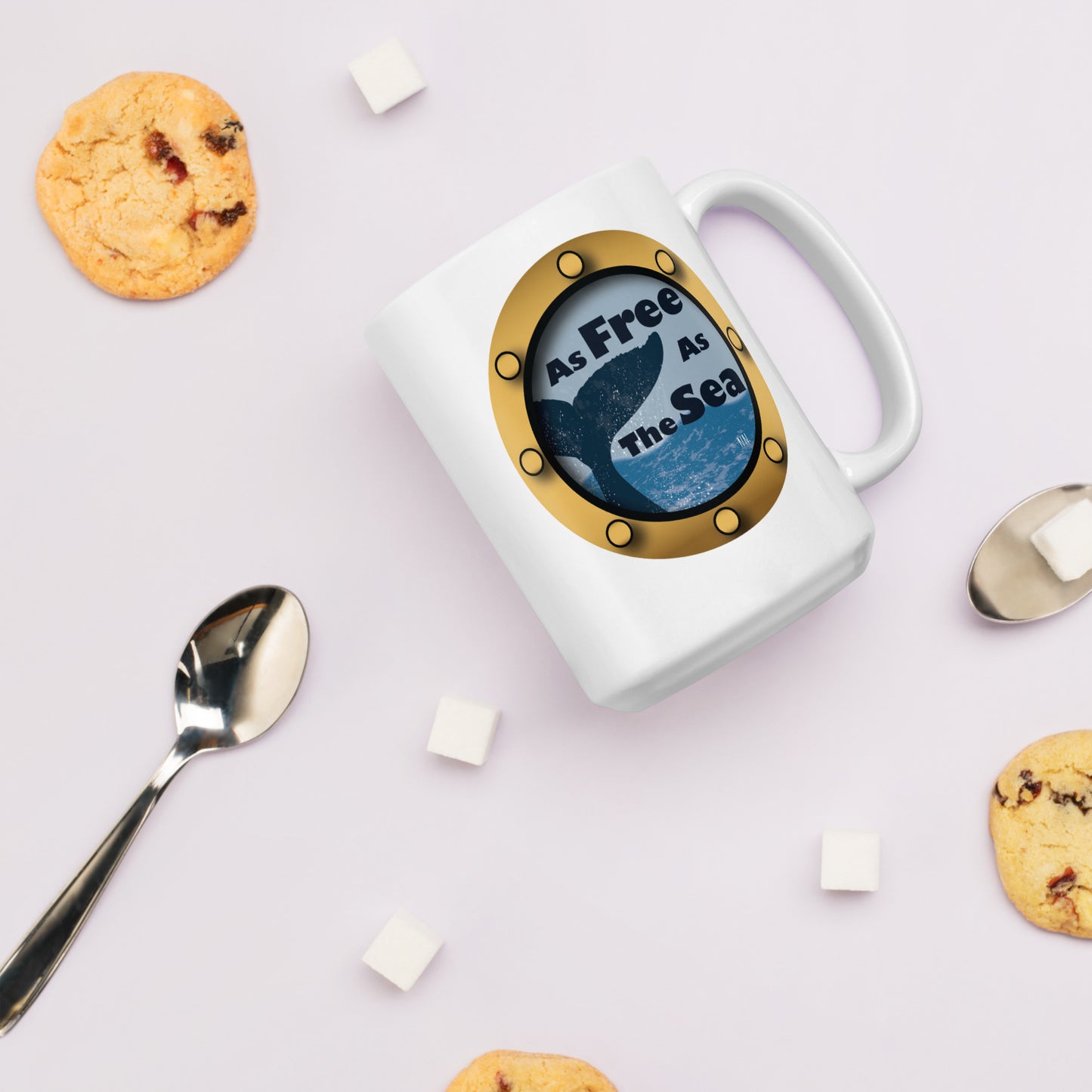 White mug with a whale and sea graphic and 'Free as the Sea' text on a light pink background with cookies and a spoon.