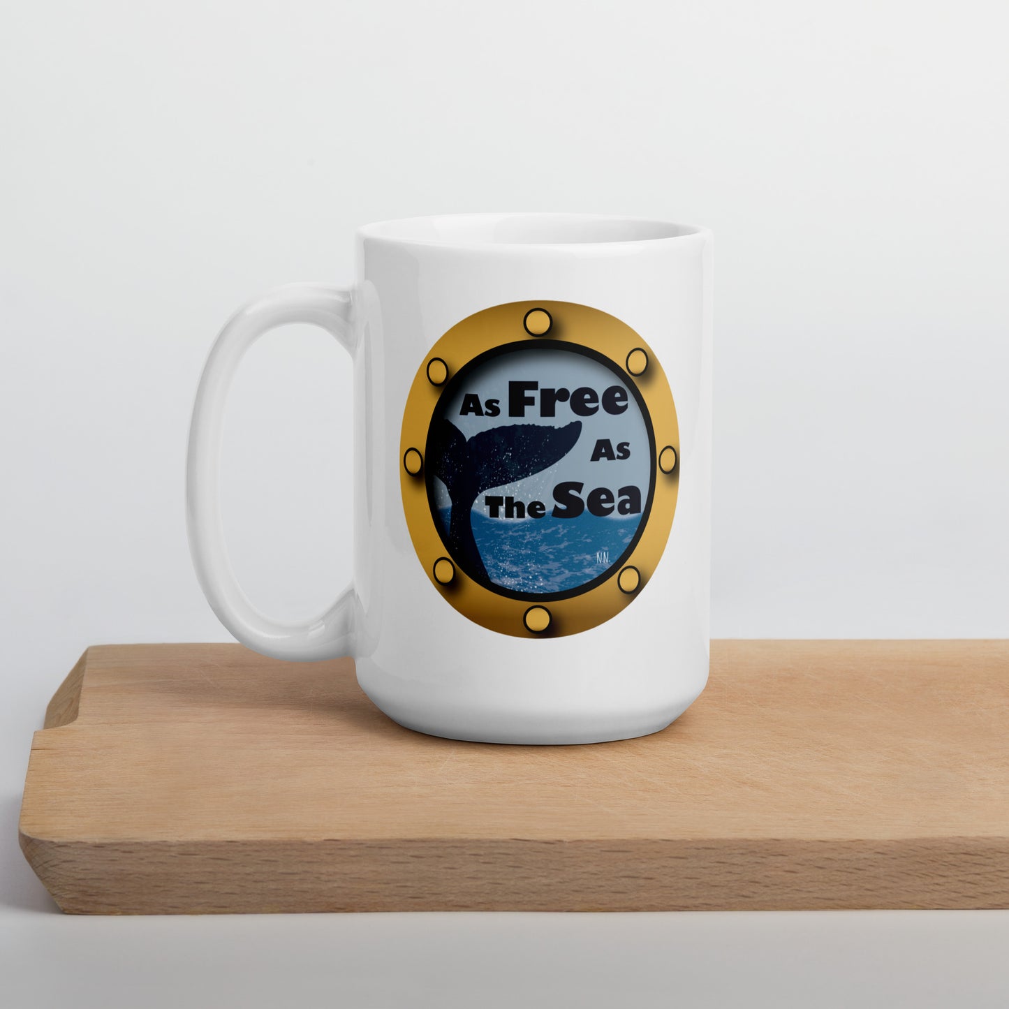 White mug with a whale and sea graphic and 'Free as the Sea' text  on a wooden surface.