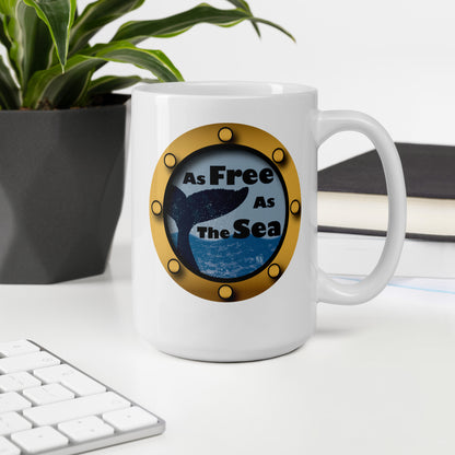 White mug with a whale and sea graphic and 'Free as the Sea' text on a desk with a plant and books.