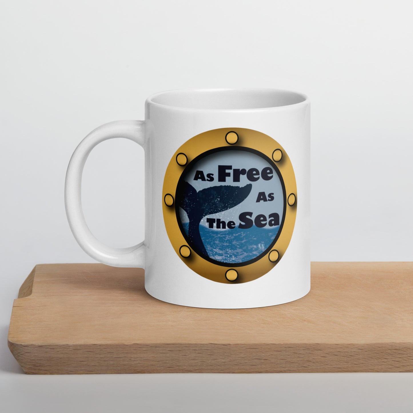 White mug with a whale and sea graphic and 'Free as the Sea' text on a wooden surface.