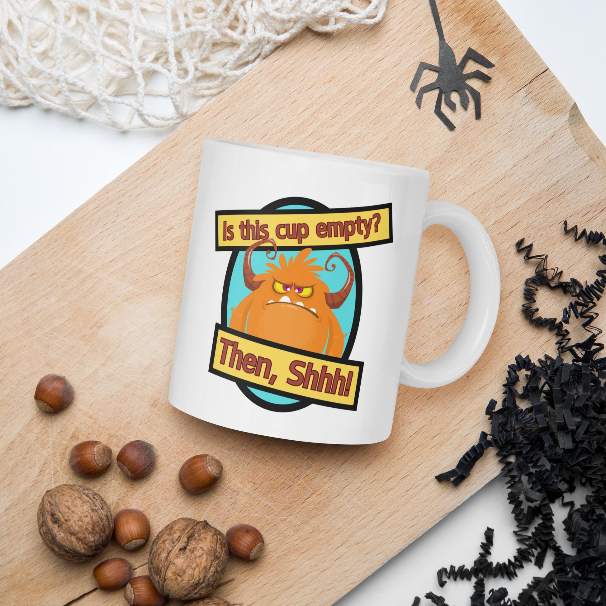 White Wizard Prints funny mug with cartoon monster and 'Is this cup empty? Then Shhh!' text on a wooden board with nuts and spider decorations