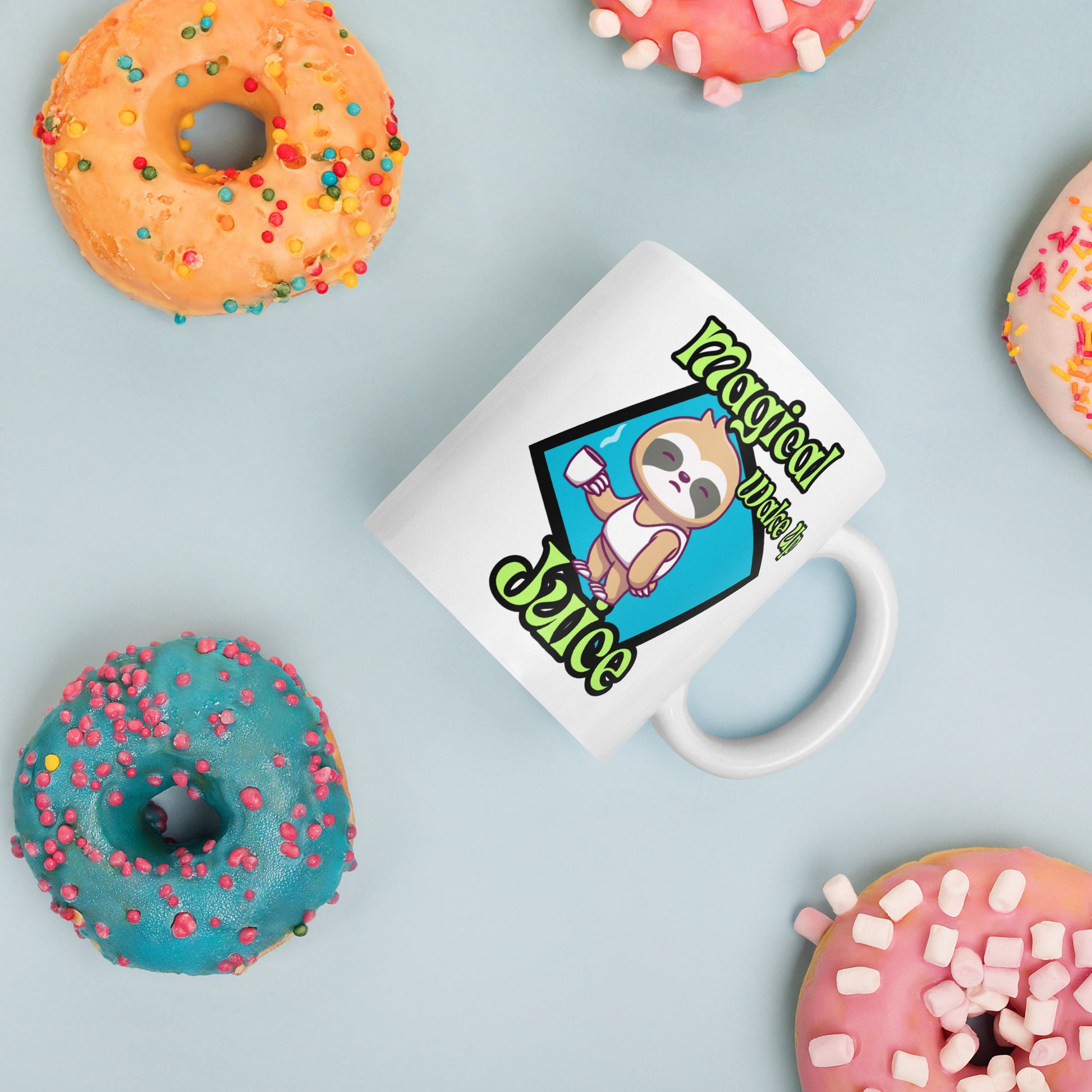 White Wizard Prints mug with a cartoon sloth design and 'Magical Wake up Juice' text surrounded by colorful donuts on a light blue background