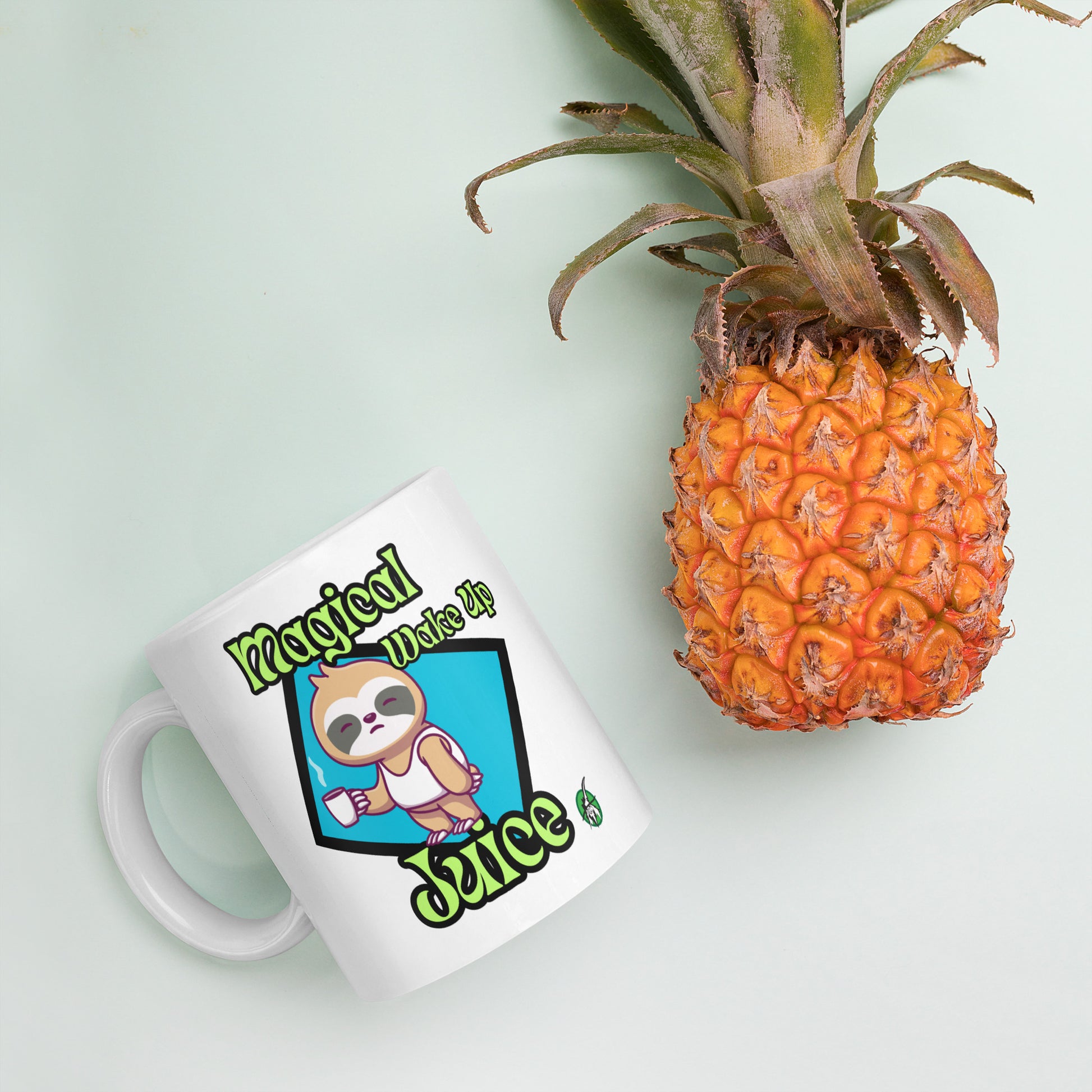 White Wizard Prints mug with a cartoon sloth design and 'Magical Wake up Juice' text and pineapple on a light green background