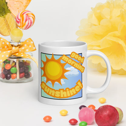 White Wizard Prints mug with 'Good morning sunshine' text and sunny graphic, surrounded by colorful candies and flowers on a white background.