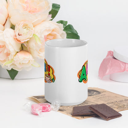 White mug with colourful design featuring a coffee cup and 'Ahhh!' text, placed on a surface with flowers and snacks.