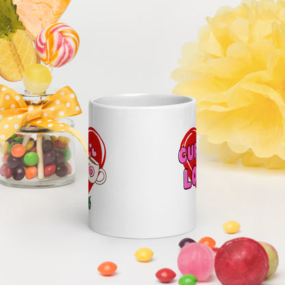 White Wizard Prints mug with a love heart design and 'Cuppa Love' text surrounded by colourful candies and flowers on a white background.