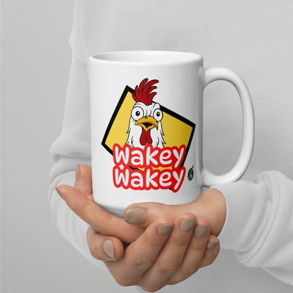 A Wizard Prints white mug with 'Wakey Wakey' text and cartoon rooster graphic held by a person against a gray background.