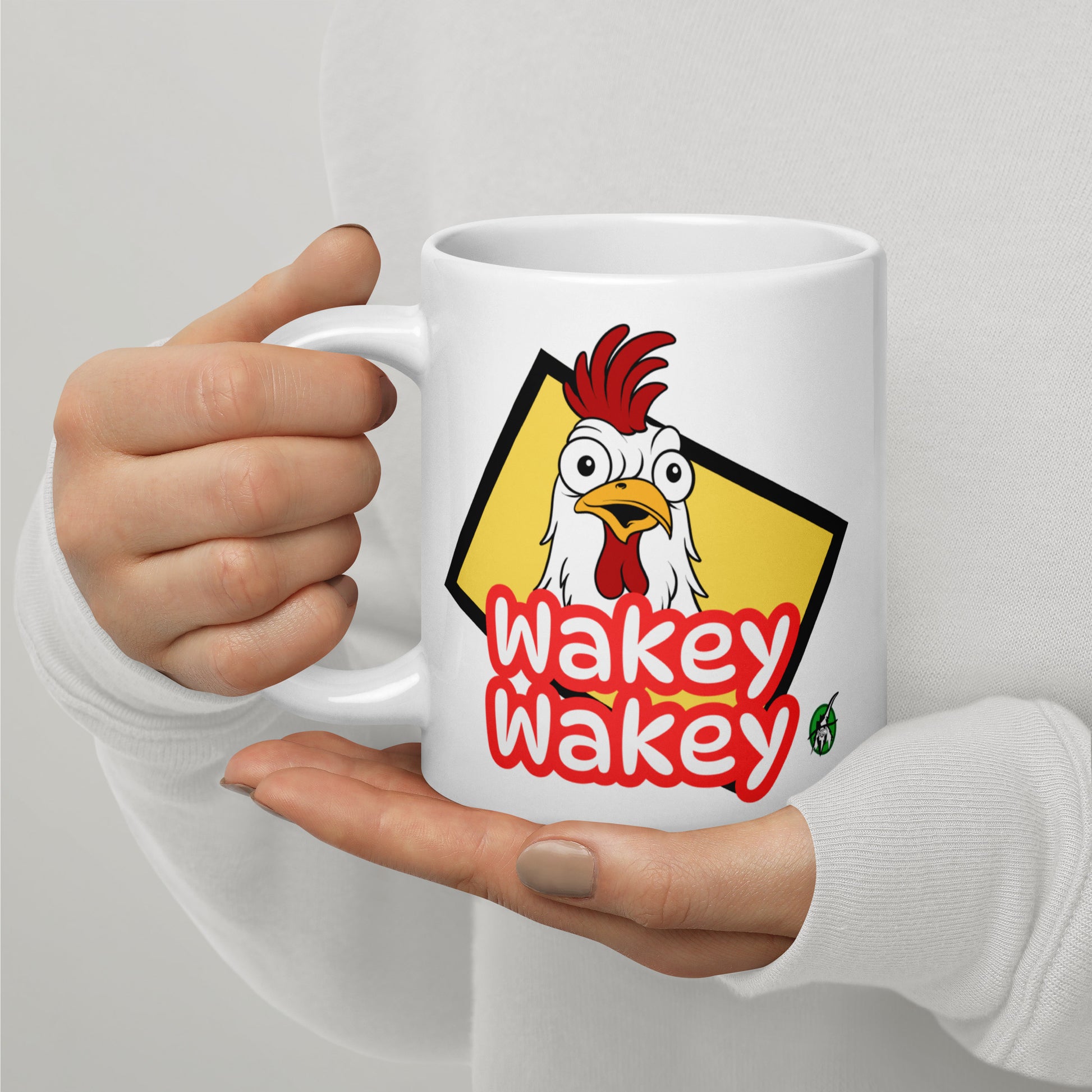 A Wizard Prints white mug with a cartoon rooster graphic and 'Wakey Wakey' text held by a person against a light grey background.