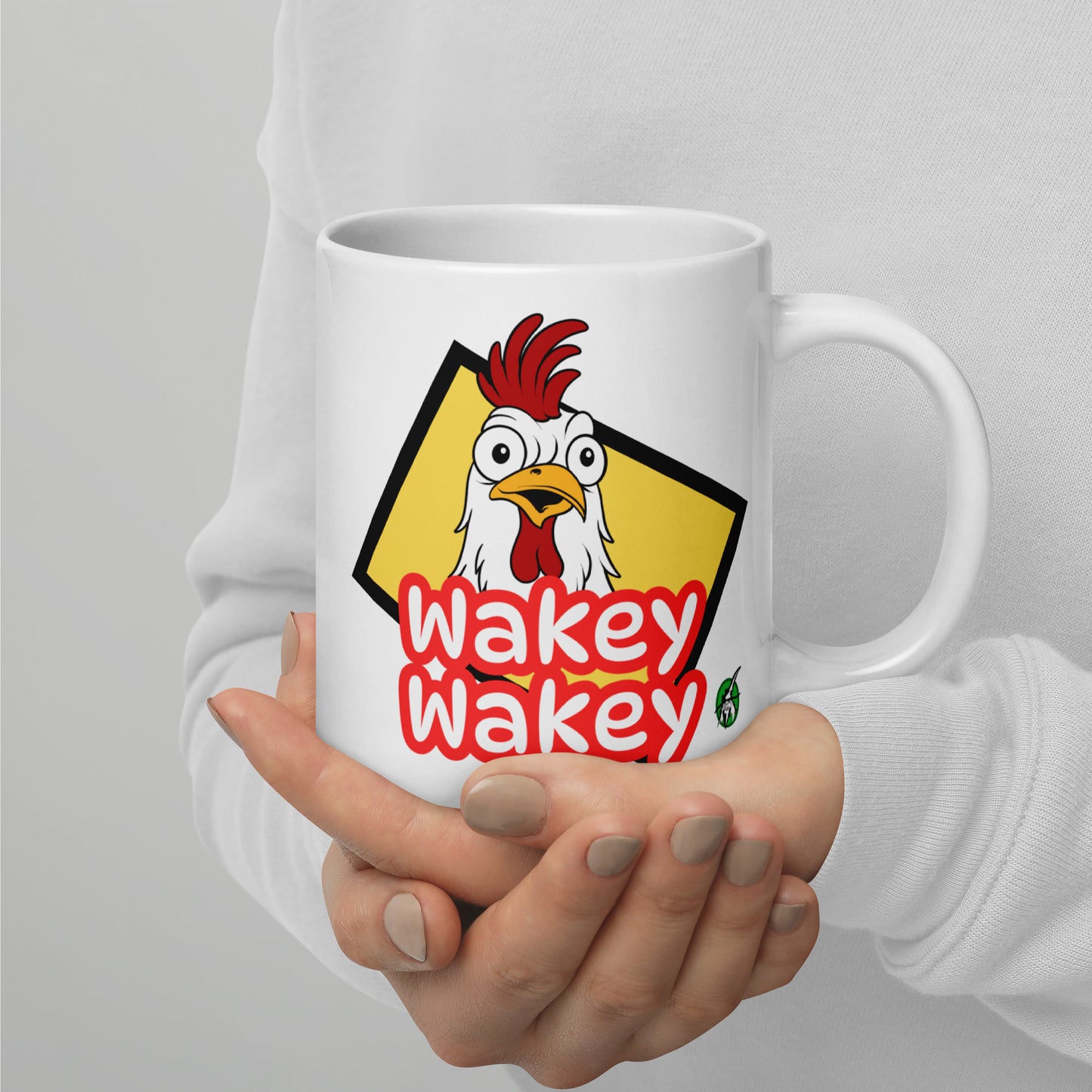 A Wizard Prints white mug with a cartoon rooster and 'Wakey Wakey' text held by a person against a light grey background.