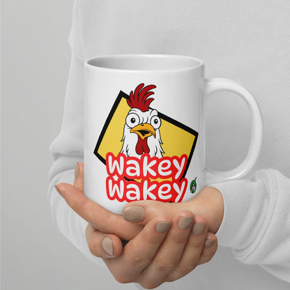 A Wizard Prints white mug with a cartoon rooster and 'Wakey Wakey' text held by a person against a light grey background.