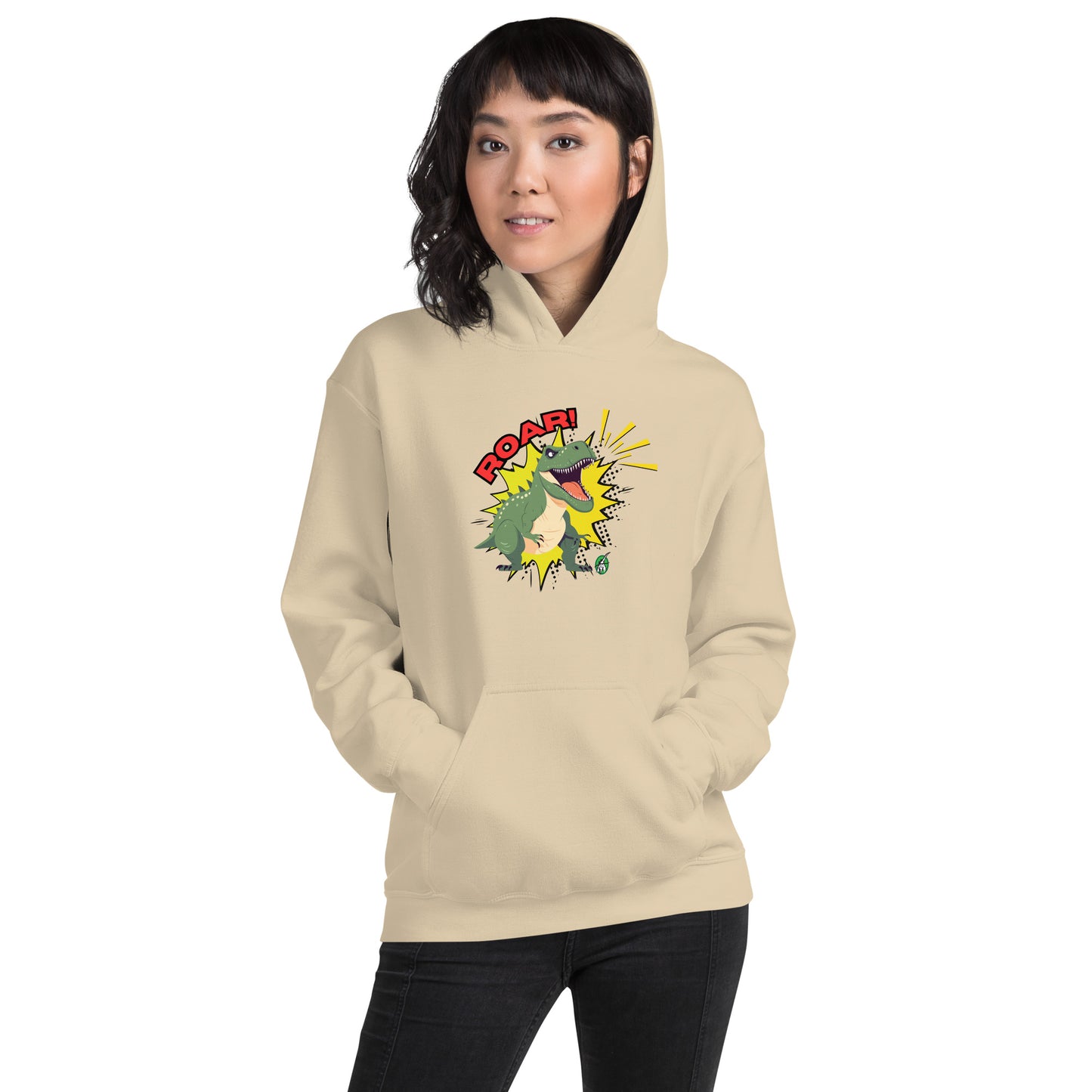 A woman standing wearing a beige hoodie with a printed graphic of a green roaring cartoon dinosaur and the word Roar! Designed by Wizard Prints