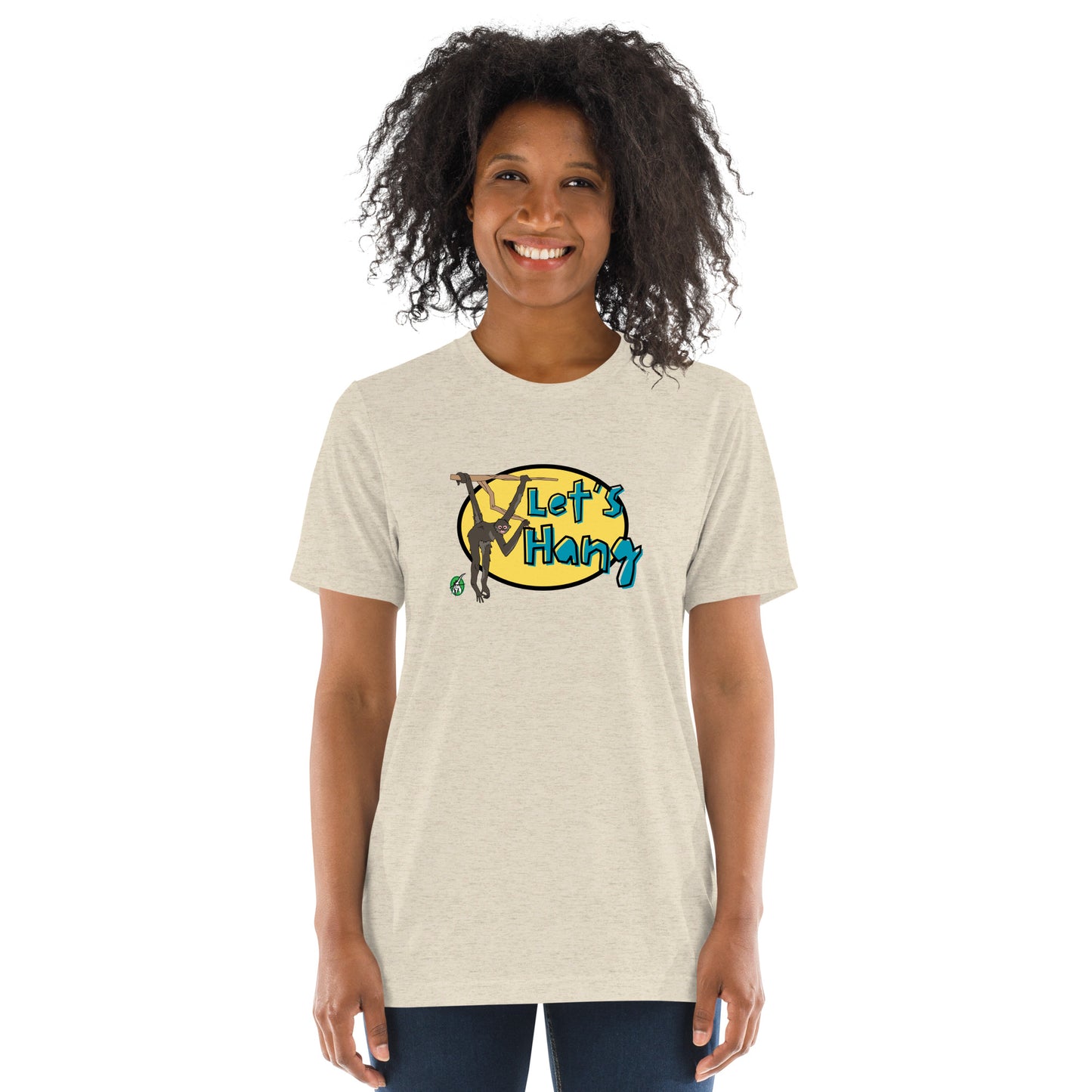 A woman standing wearing a beige tee shirt with a printed graphic of a monkey hanging on a branch with the words, Let's Hang. Designed by Wizard Prints