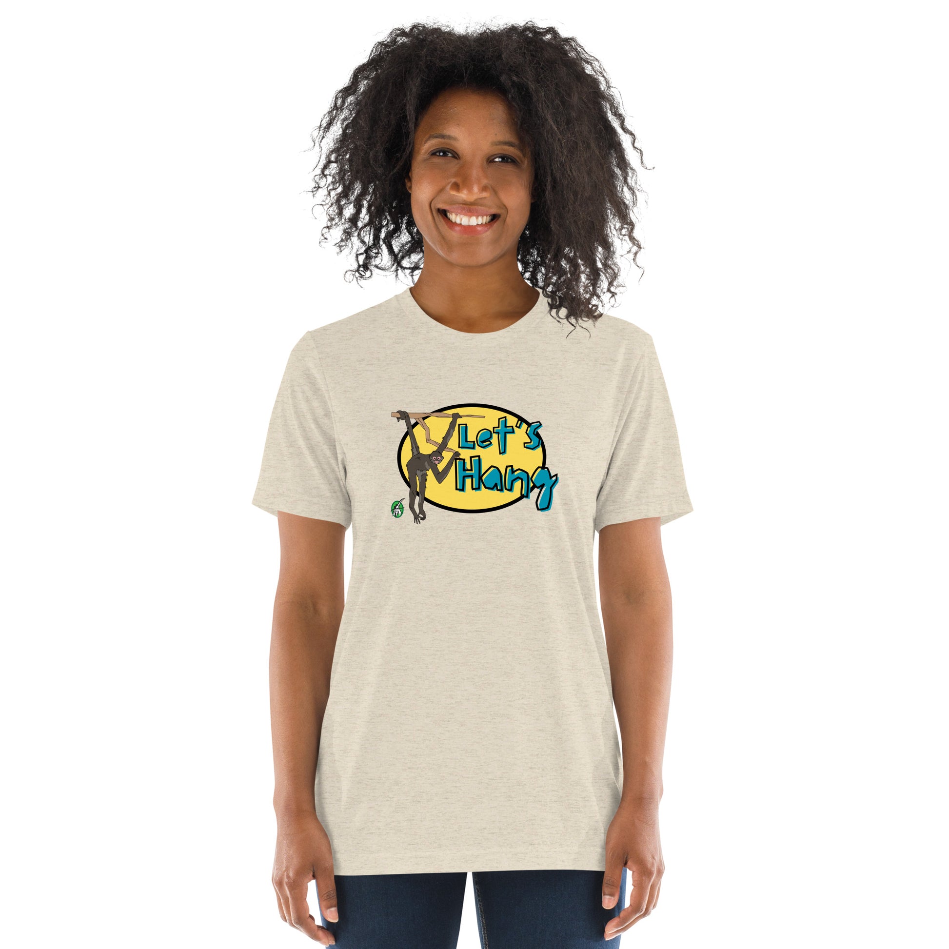 A woman standing wearing a beige tee shirt with a printed graphic of a monkey hanging on a branch with the words, Let's Hang. Designed by Wizard Prints