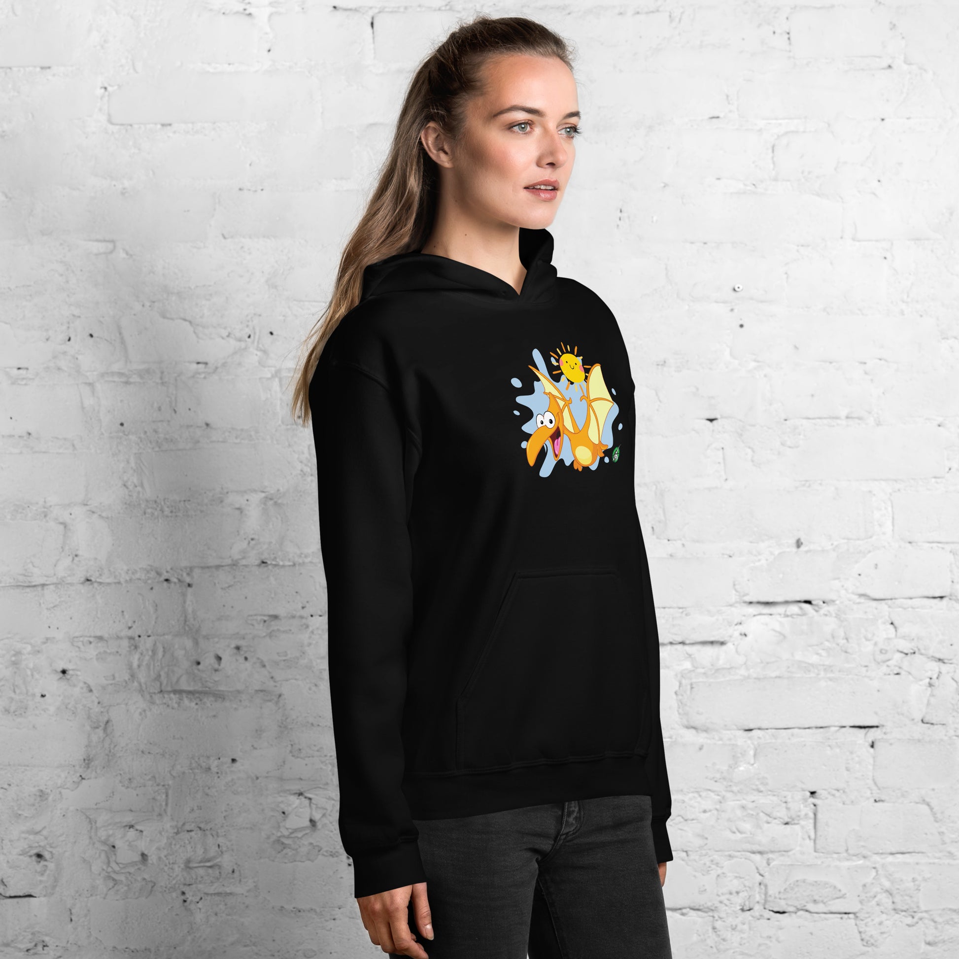 A woman standing wearing a black hoodie with a printed graphic of a smiling cartoon dinosaur and the sun. Designed by Wizard Prints.