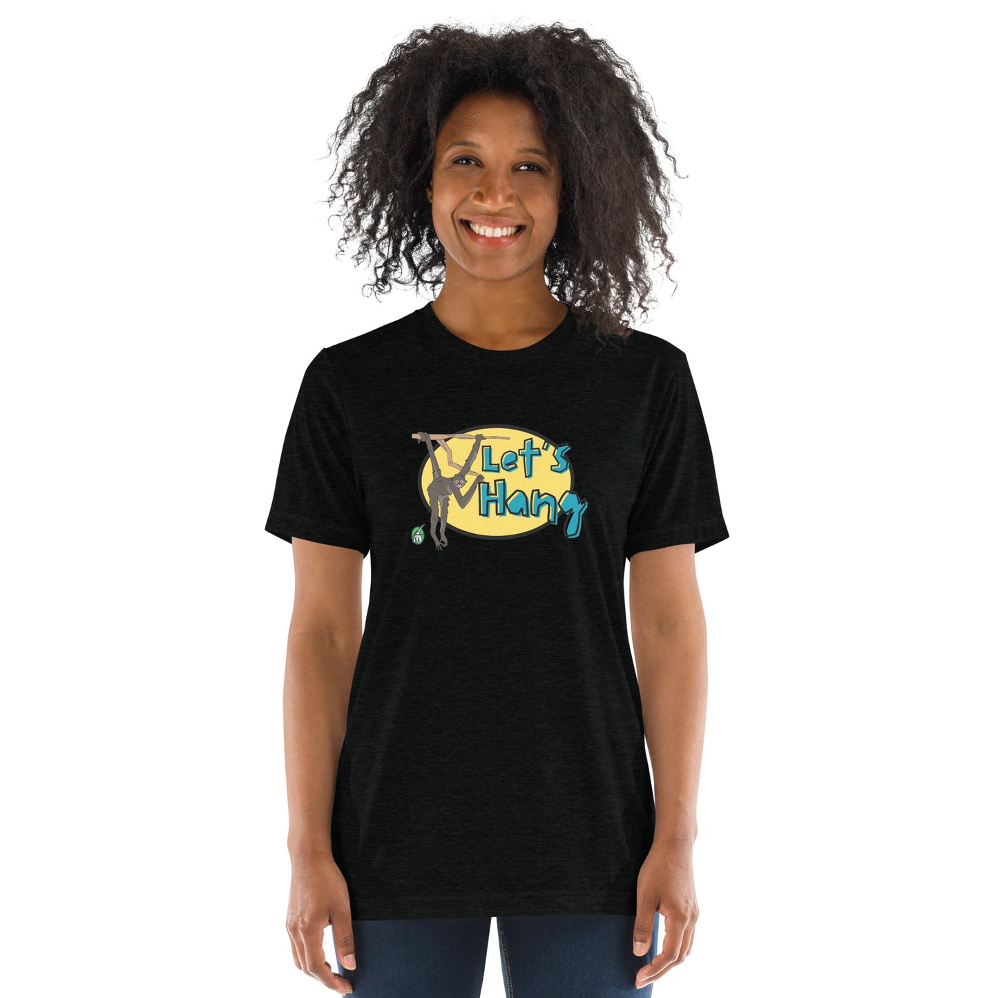 A woman standing wearing a black tee shirt with a printed graphic of a monkey hanging on a branch with the words, Let's Hang. Designed by Wizard Prints
