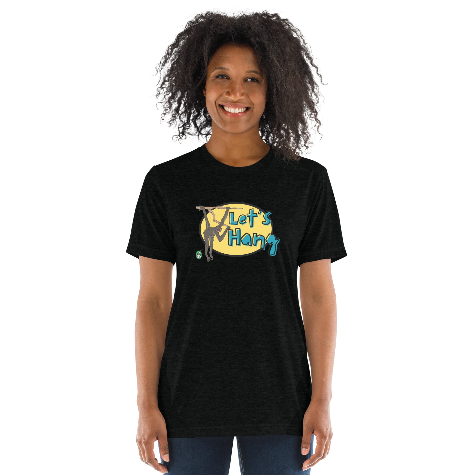 A woman standing wearing a black tee shirt with a printed graphic of a monkey hanging on a branch with the words, Let's Hang. Designed by Wizard Prints