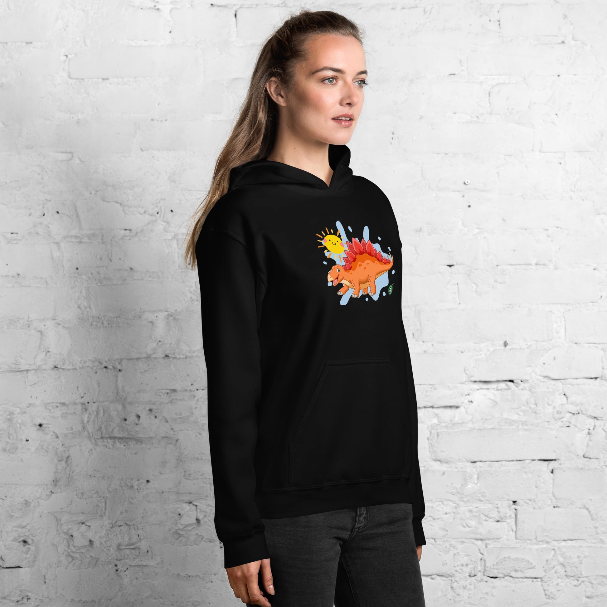 A woman standing wearing a black hoodie with the printed graphic of an orange cartoon dinosaur and the sun, by Wizard Prints.