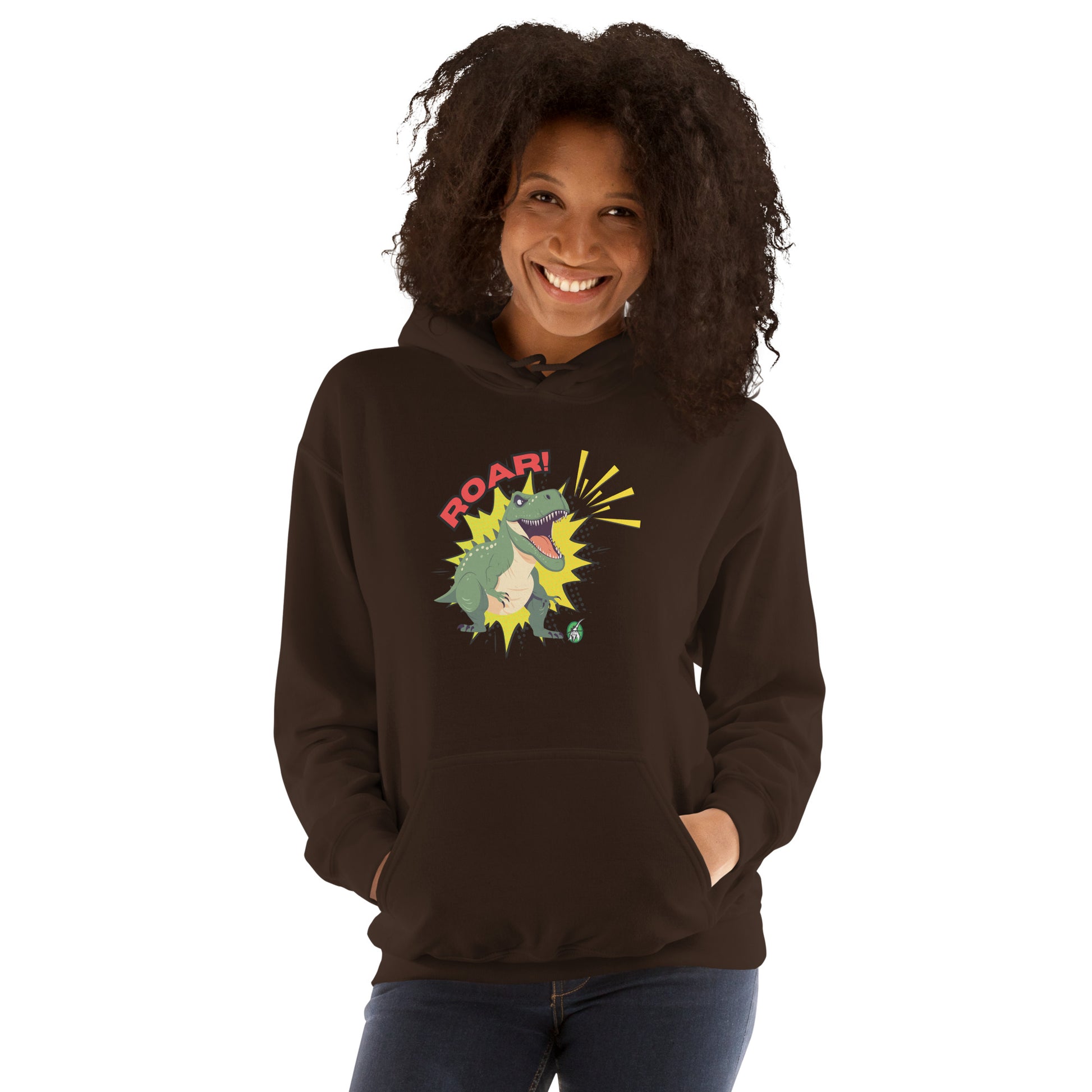 A woman standing wearing a brown hoodie with a printed graphic of a green roaring cartoon dinosaur and the word Roar! Designed by Wizard Prints