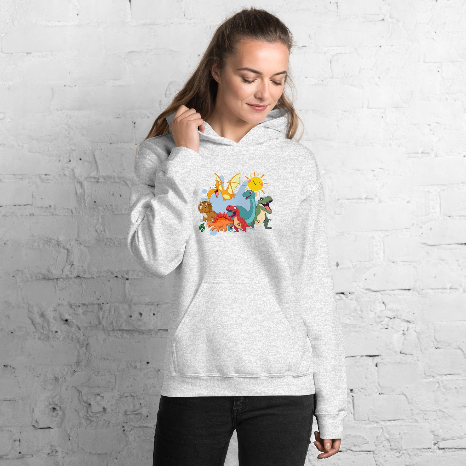 A woman standing wearing an ash hoodie with a printed graphic of different colorful dinosaur types and the sun. Designed by Wizard Prints.
