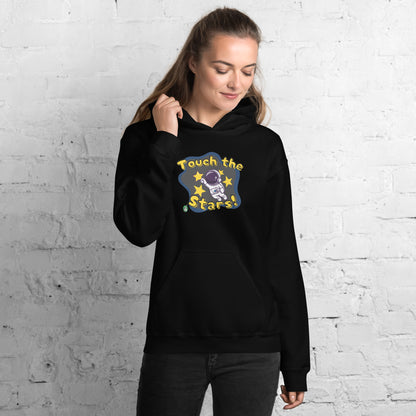 A woman standing wearing a black hoodie with a printed graphic of a cartoon astronaut and the words, Touch the Stars. Designed by Wizard Prints.