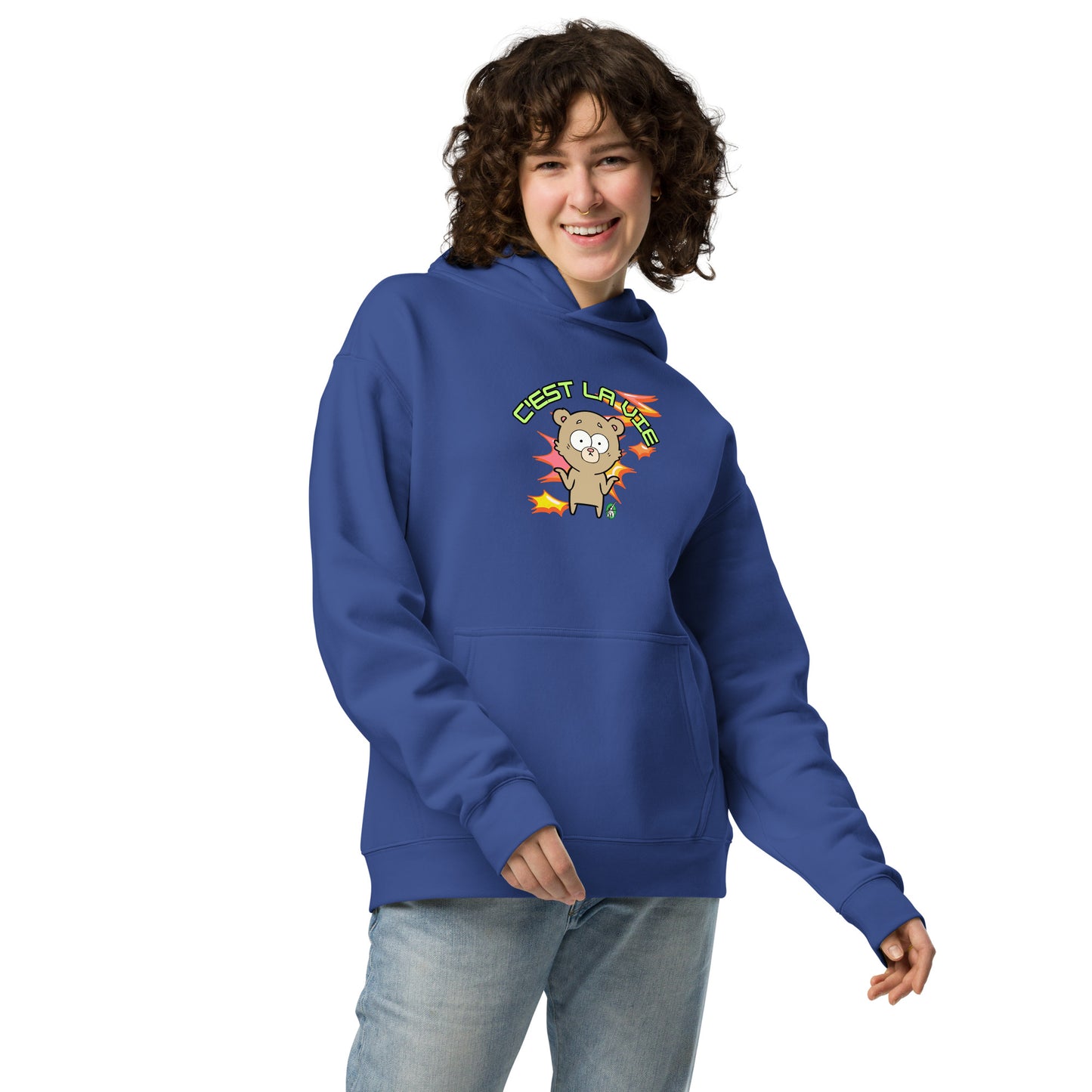 A woman standing wearing a blue hoodie by Wizard Prints featuring a printed graphic of a shrugging cartoon bear and the words, C'est La Vie.