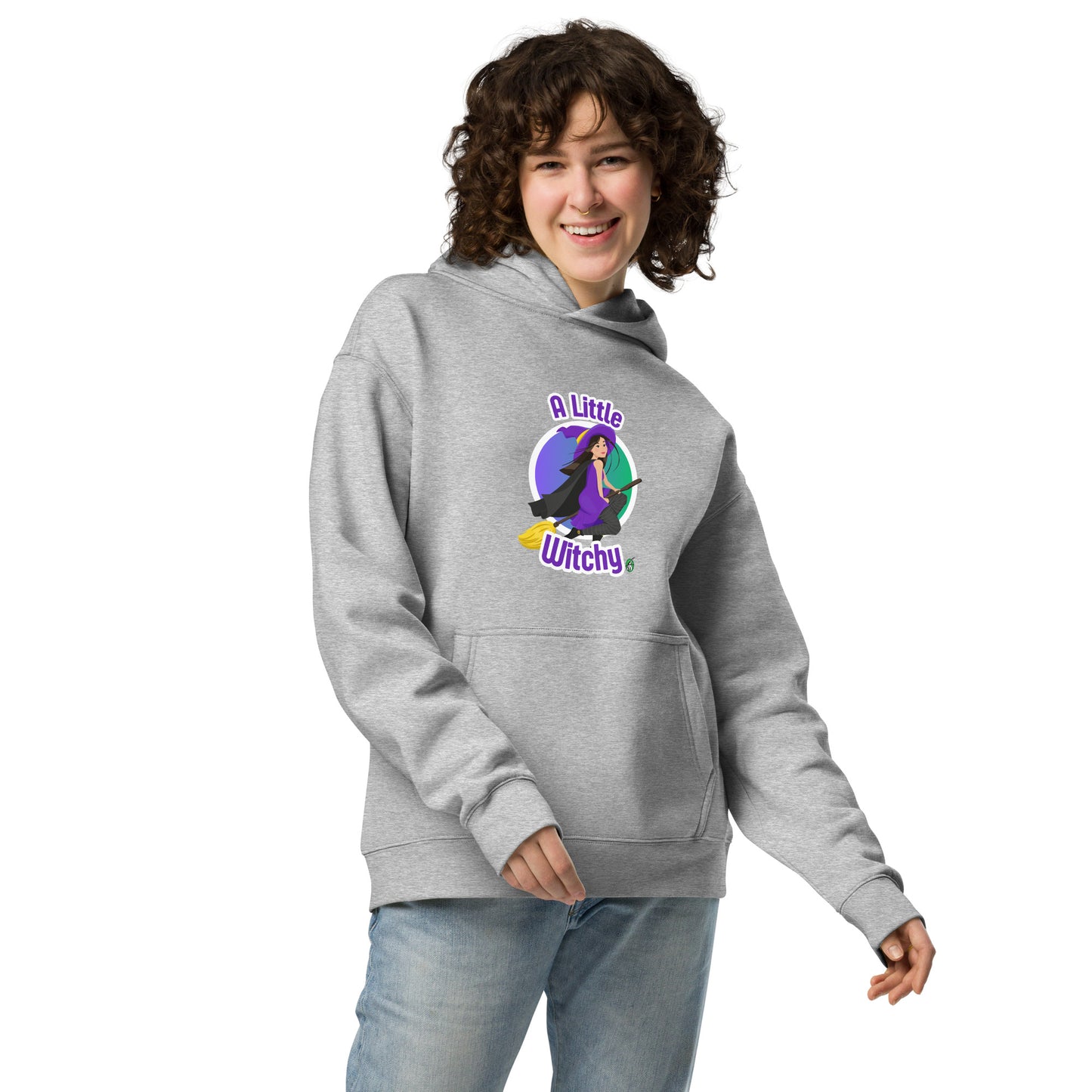 A woman standing wearing a grey hoodie by Wizard Prints featuring a printed graphic of a witch riding a flying broom, with the text, A Little Witchy.