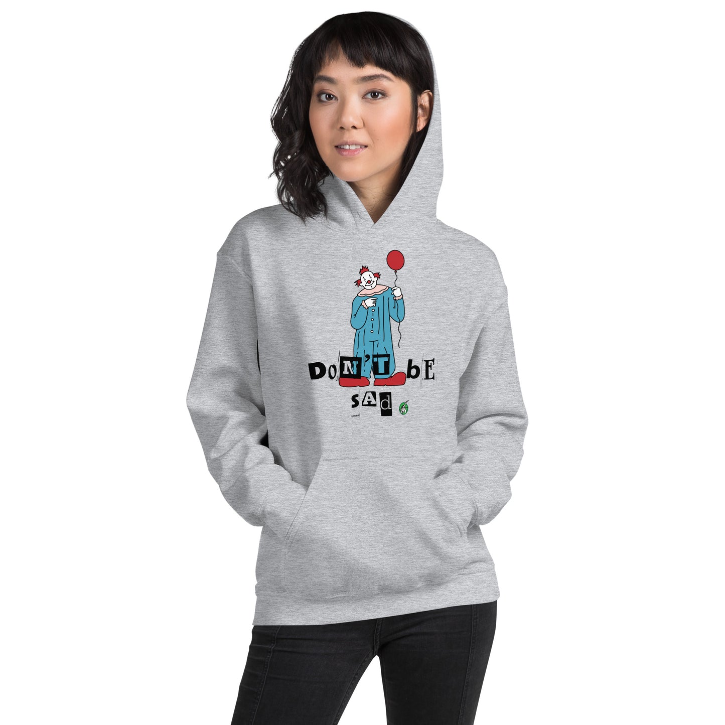 A woman standing and wearing a grey hoodie with a printed graphic of a clown holding a balloon with the words, 'Don't Be Sad'. Designed by Wizard Prints.