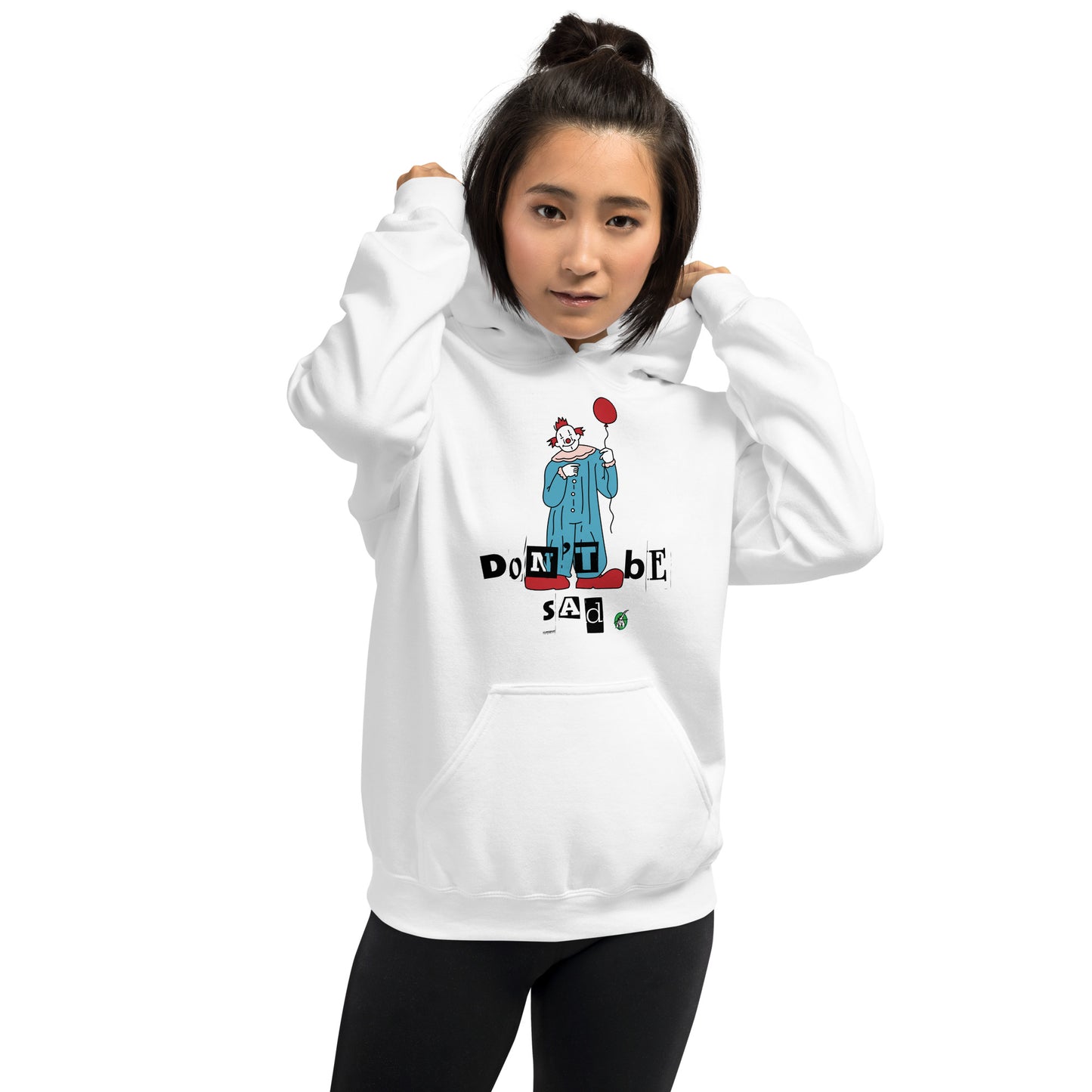 A woman standing and wearing a white hoodie with a printed graphic of a clown holding a balloon with the words, 'Don't Be Sad'. Designed by Wizard Prints.