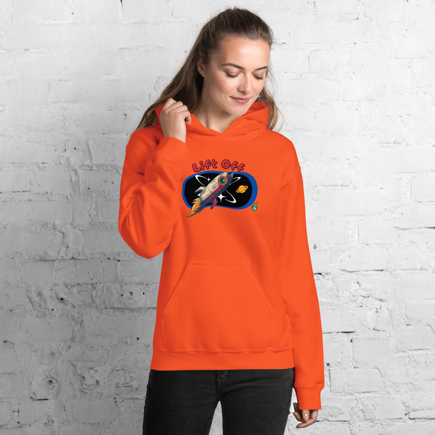 A woman standing wearing an orange hoodie with a printed graphic of a rocket and the words, Lift Off. Designed by Wizard Prints.