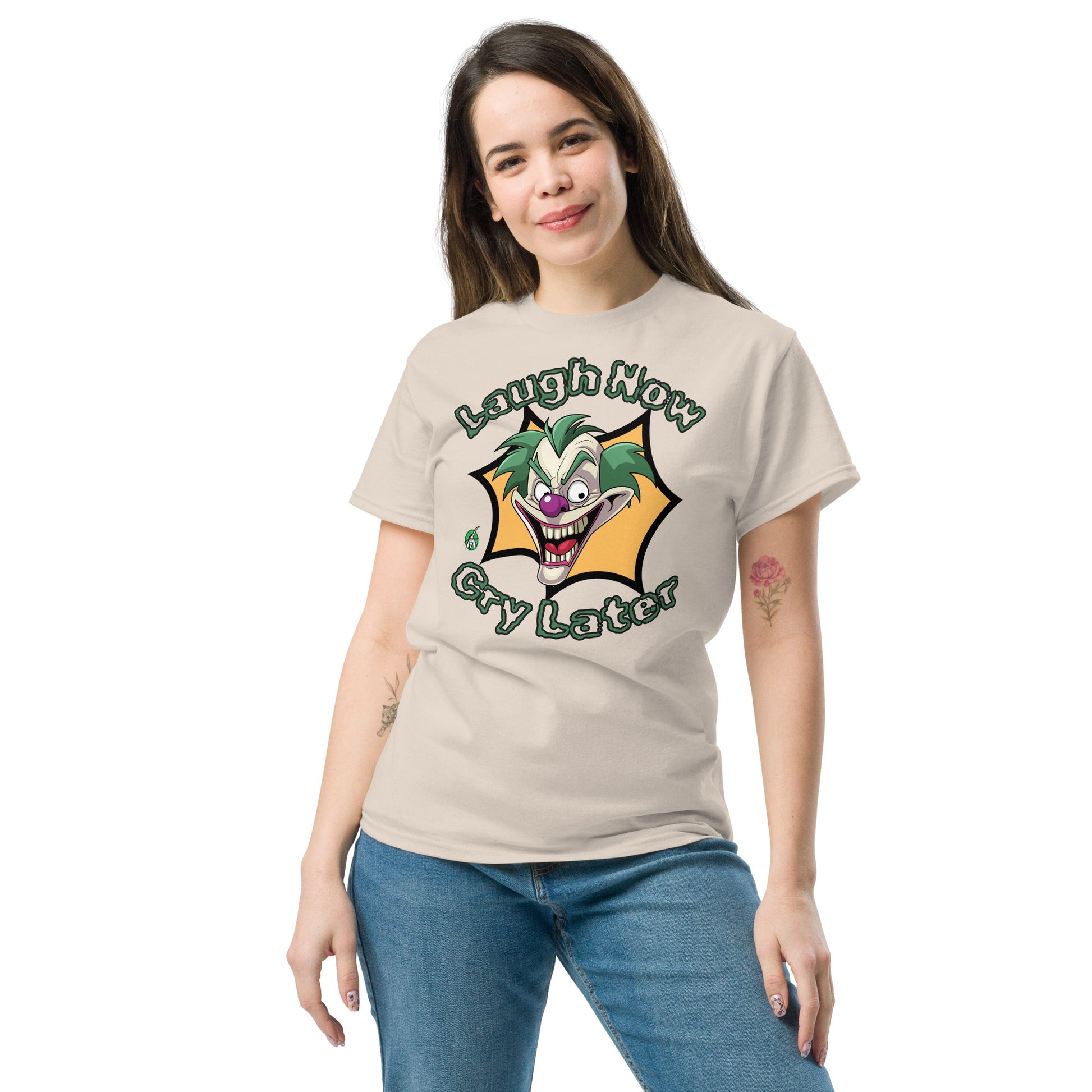 A woman standing wearing a beige t-shirt with a printed graphic of a clown with the words, 'Laugh Now, Cry Later'. Designed by Wizard Prints.