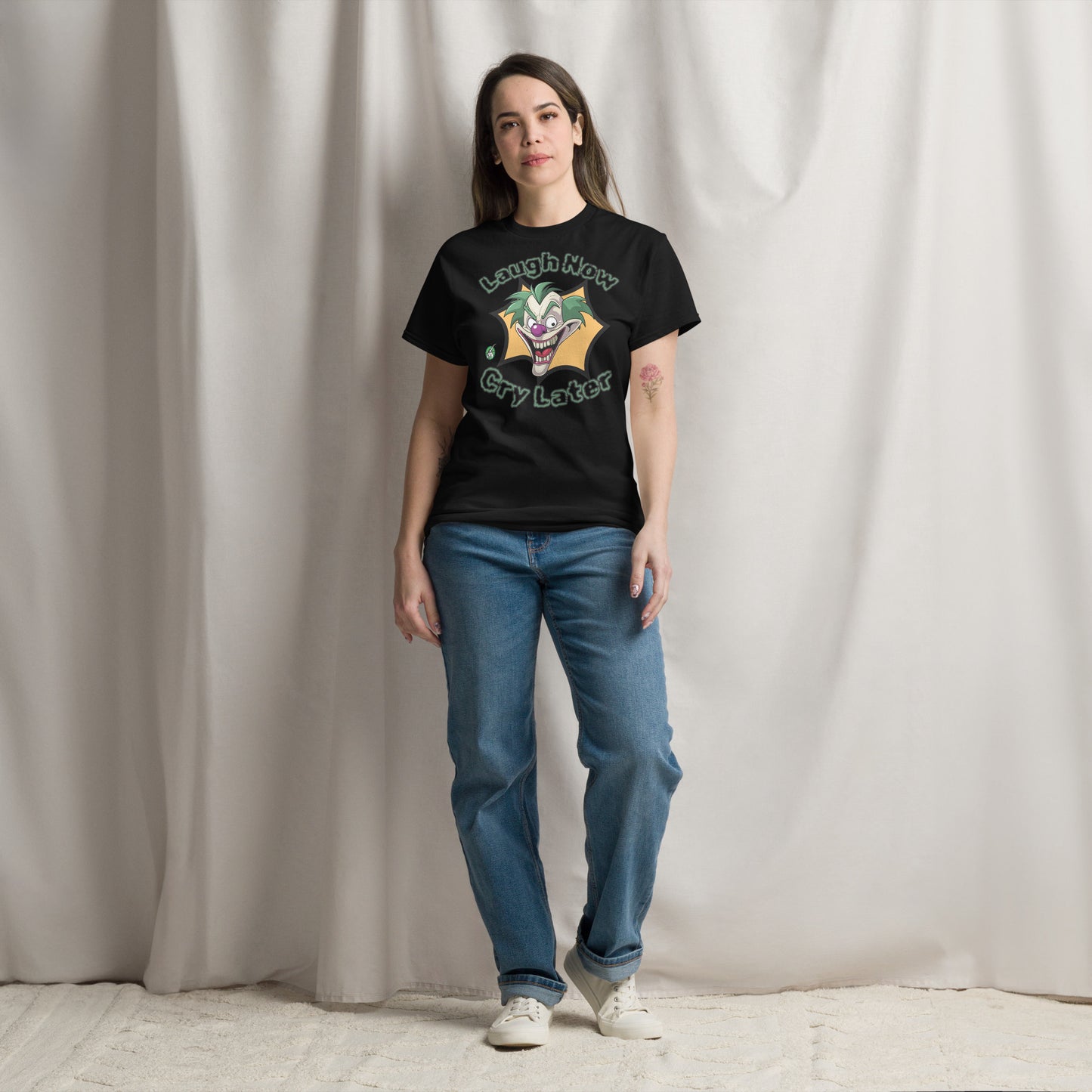 A woman standing wearing a black t-shirt with a printed graphic of a clown with the words, 'Laugh Now, Cry Later'. Designed by Wizard Prints.
