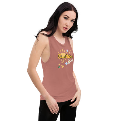 A woman standing wearing a mauve tank top by Wizard Prints with a printed graphic of a the sun, flowers and the stars with the words, 'Good Vibes'.